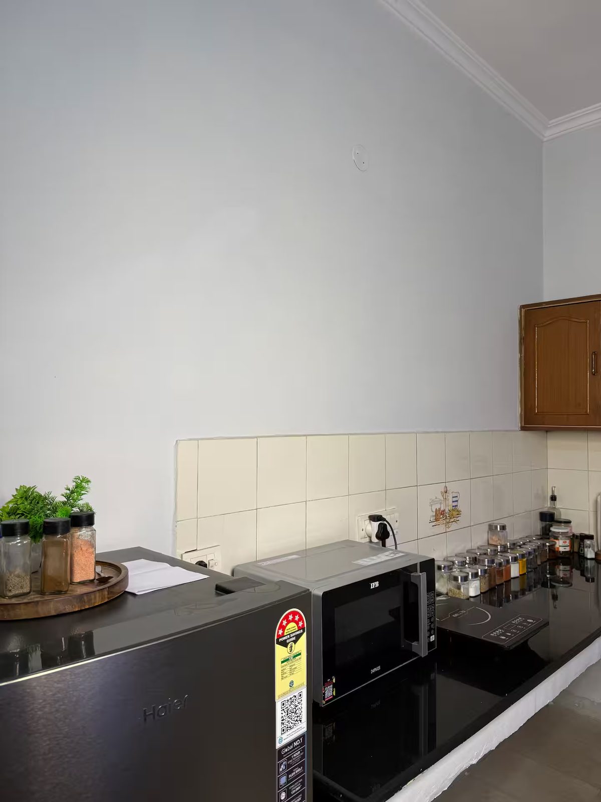 Kitchen with L-shaped black countertops, wooden wall cabinets, a microwave, air fryer, electric kettle, spice jars, utensil holders, and wall-mounted kitchen tools.