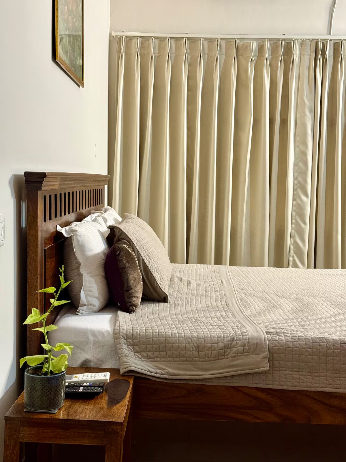 Bedroom with a wooden bed, white quilt and pillows, bedside tables, floor-to-ceiling curtains, wall-mounted air conditioner, framed artwork, and decorative ceiling molding.