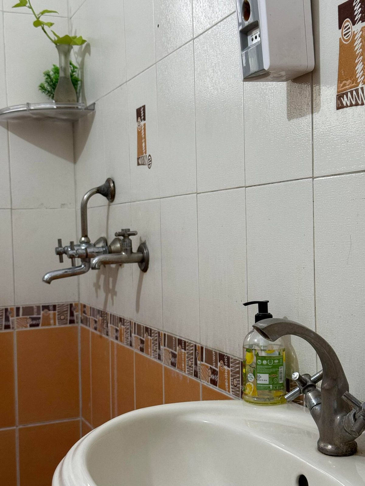 White towel hanging on a chrome towel bar against beige tiled bathroom walls, with a small decorative tile pattern above.